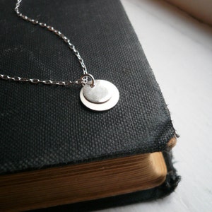 May include: A silver necklace with a double circle pendant. The necklace is on a black book.
