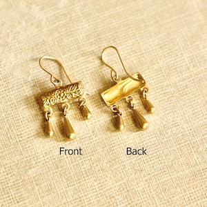 May include: A pair of gold-toned metal earrings featuring a rectangular bar with an embossed floral pattern and three dangling teardrop-shaped charms. One earring shows the detailed front, while the other displays the smooth, plain back side.