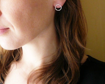 Puede incluir: Primer plano de la oreja de una mujer con un pequeño pendiente de círculo plateado. El pendiente es simple y elegante, con un acabado liso y pulido.