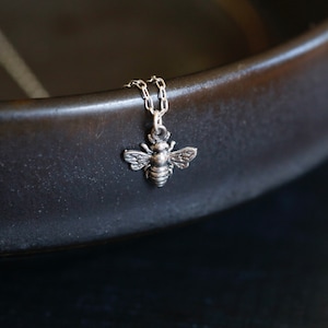 May include: A silver bee charm necklace with a delicate chain. The bee charm is detailed and has a realistic appearance.