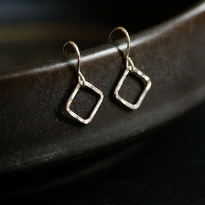 May include: A pair of silver earrings with a hammered diamond shape.