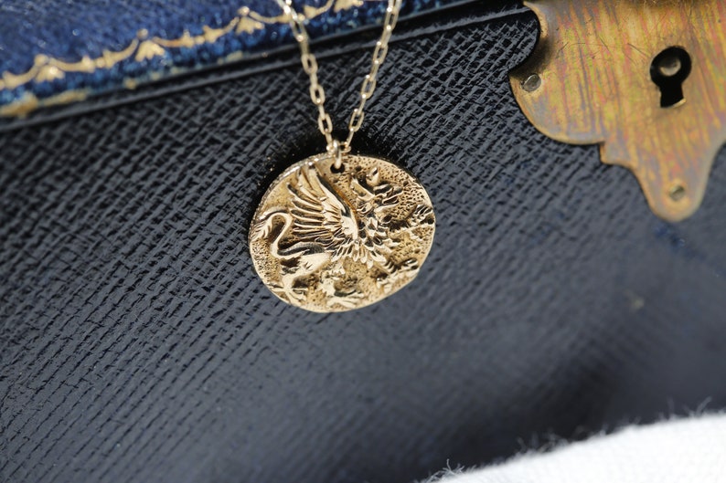 Op de afbeelding: Een gouden ketting met een ronde hanger met een gedetailleerd, reli&euml;fbeeld van een gevleugelde leeuw.