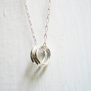 May include: A silver necklace featuring a pendant with three interlocking rings. The pendant hangs from a delicate chain. The jewelry is displayed against a white background, highlighting the necklace's design.