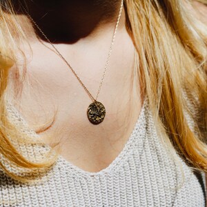 Op de afbeelding: Een gouden ketting met een getextureerde ronde hanger.
