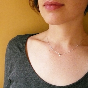 May include: A silver chain necklace with a small, round, clear gemstone pendant.