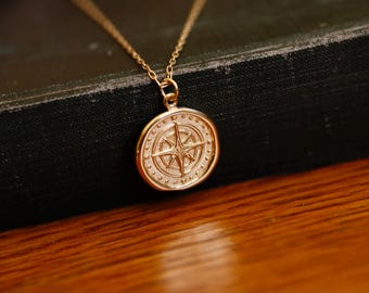 May include: A gold compass pendant necklace with a detailed design. The compass features a star in the centre and is surrounded by a circle of small dots.