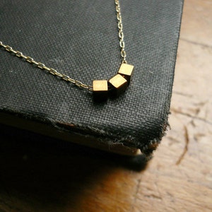 May include: A gold chain necklace with a pendant made of three small gold cubes.