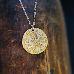 Op de afbeelding: Een gouden ketting met een ronde hanger met een gedetailleerd reli&euml;f van een griffioen.