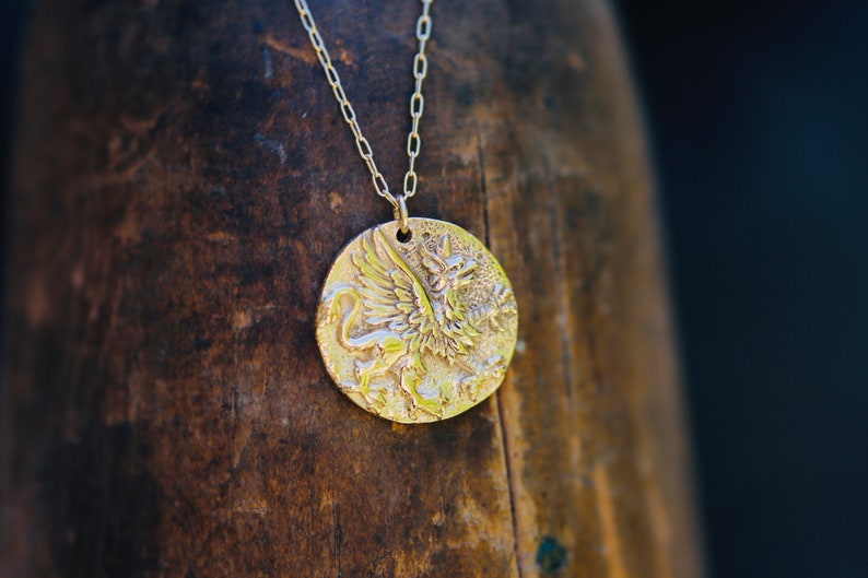Op de afbeelding: Een gouden ketting met een ronde hanger met een gedetailleerd reli&euml;f van een griffioen.