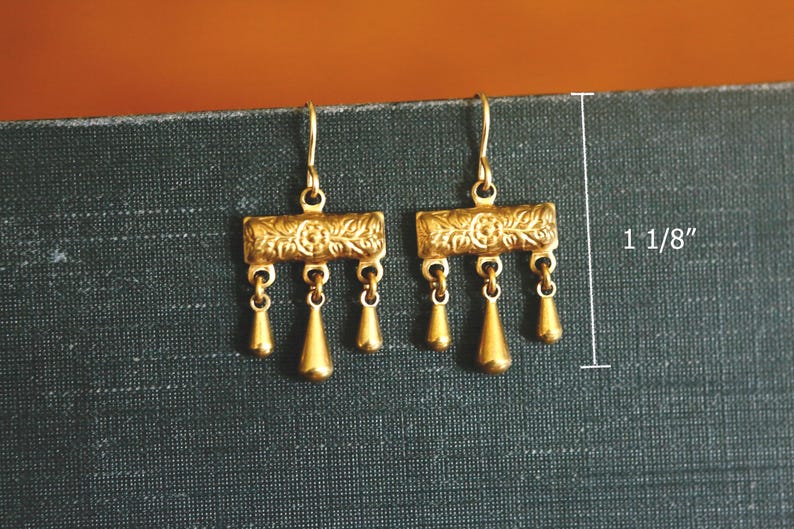 May include: A pair of gold-toned drop earrings featuring a rectangular bar with an embossed floral pattern and three dangling teardrop charms. The earrings measure 1 1/8 inches in total length and are suspended from simple curved ear wires.