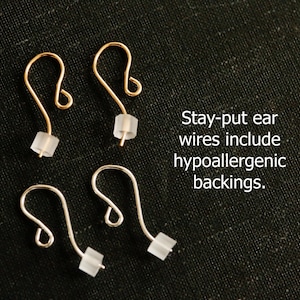 May include: Two pairs of ear wires, one gold-toned and one silver-toned, each featuring a curved hook design and a small, translucent, hypoallergenic backing. The text reads: Stay-put ear wires include hypoallergenic backings.