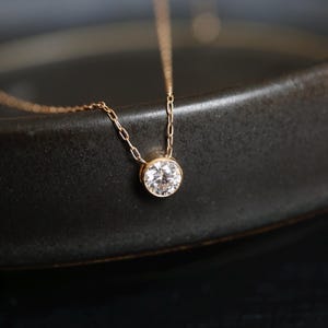 May include: A delicate gold chain necklace with a small, round, clear gemstone pendant.