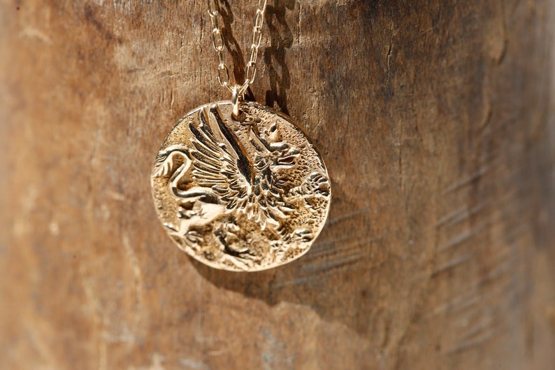 A small gold rustic coin necklace. Reproduction of a Greek coin, featuring the mystical Griffin, a mixture between a lion and an eagle - lion's body with eagle wings. Considered the king of the animals and the king of beasts.