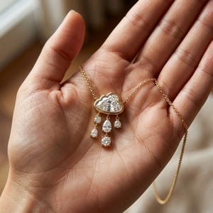 Könnte beinhalten: Eine goldene Halskette mit einem wolkenförmigen Anhänger, besetzt mit einem großen zentralen Diamanten und kleineren Diamanttropfen. Die Halskette wird in einer Hand präsentiert, um das filigrane Design und die feinen Details des Schmucks hervorzuheben.