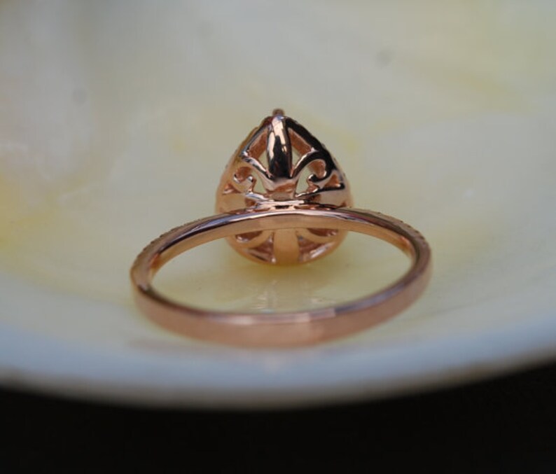 Puede incluir: Un anillo de compromiso de oro rosa con un engaste abierto en forma de pera. El anillo tiene un dise&ntilde;o delicado y filigrana.