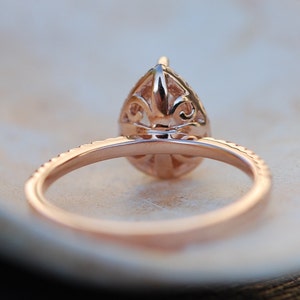 May include: Rose gold engagement ring with a pear-shaped diamond set in a delicate filigree design. The band is accented with smaller diamonds.