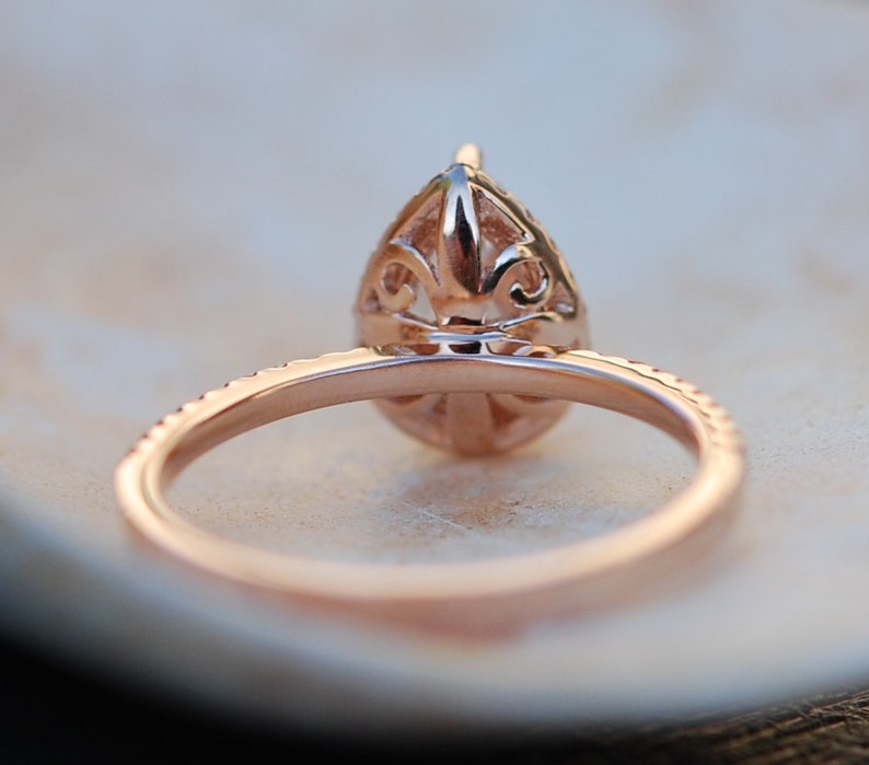 May include: Rose gold engagement ring with a pear-shaped diamond set in a delicate filigree design. The band is accented with smaller diamonds.