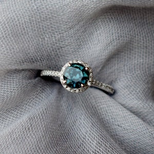 May include: A silver ring featuring a blue gemstone set in a halo of smaller diamonds.