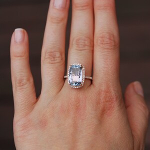 May include: A rose gold ring with a large, light blue, cushion-cut gemstone surrounded by a halo of smaller diamonds.