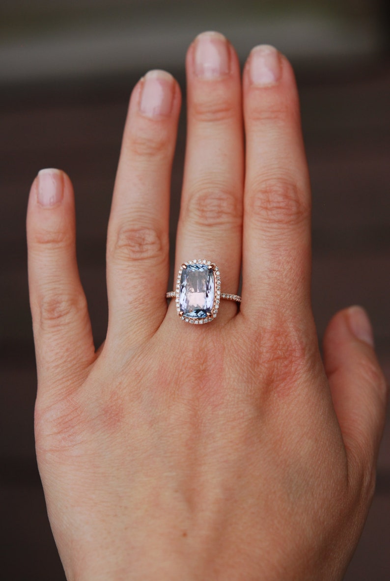 May include: A rose gold ring with a large, light blue, cushion-cut gemstone surrounded by a halo of smaller diamonds.