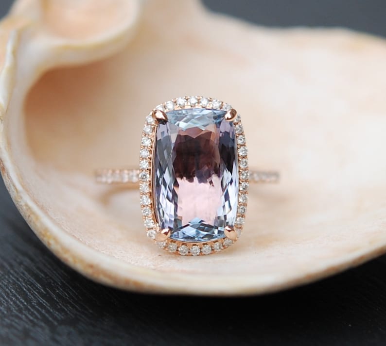 May include: A rose gold ring with a large, cushion-cut amethyst gemstone surrounded by a halo of smaller diamonds.