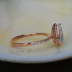 Puede incluir: Un anillo de compromiso de oro rosa con un gran diamante ovalado engastado en un halo. La banda est&aacute; adornada con diamantes m&aacute;s peque&ntilde;os.