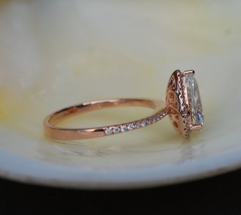 Puede incluir: Un anillo de compromiso de oro rosa con un gran diamante ovalado engastado en un halo. La banda est&aacute; adornada con diamantes m&aacute;s peque&ntilde;os.