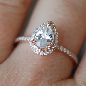 Puede incluir: Un anillo de compromiso de diamante de forma de pera con un engaste de halo y una banda pav&eacute;. El anillo est&aacute; engastado en oro rosa.