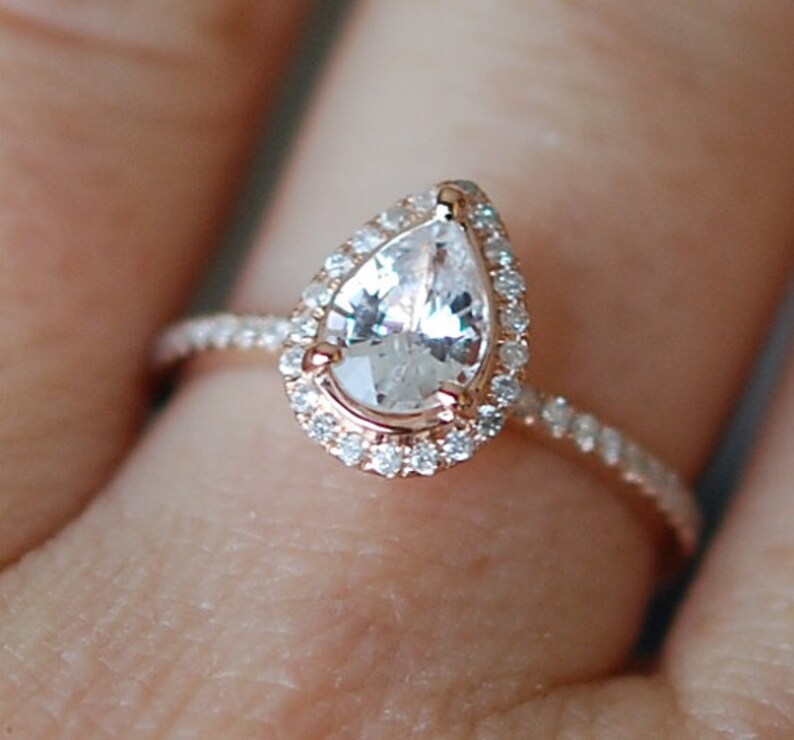 Puede incluir: Un anillo de compromiso de diamante de forma de pera con un engaste de halo y una banda pav&eacute;. El anillo est&aacute; engastado en oro rosa.