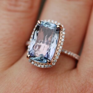 May include: A rose gold ring with a large, rectangular, light blue gemstone surrounded by a halo of smaller diamonds.