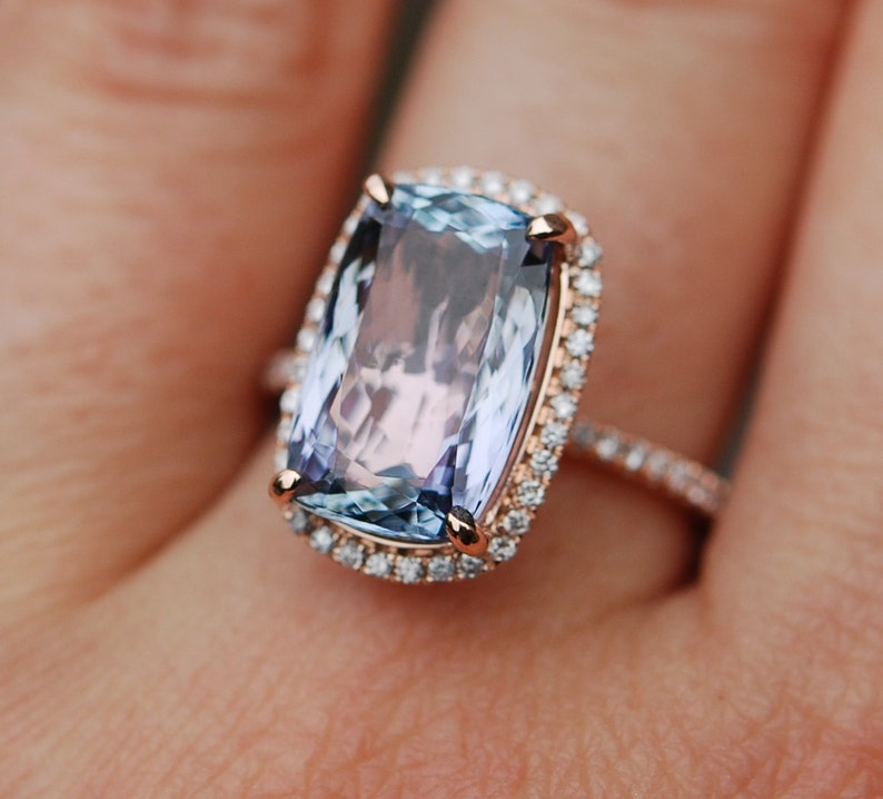 May include: A rose gold ring with a large, rectangular, light blue gemstone surrounded by a halo of smaller diamonds.