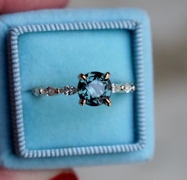 May include: A teal blue gemstone ring with a gold band and a row of small diamonds. The ring is in a light blue ring box.