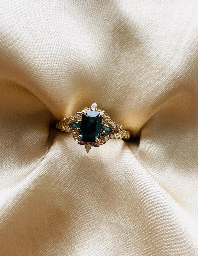 May include: A gold ring with a large emerald-cut green gemstone surrounded by smaller diamonds. The ring has a delicate floral design.