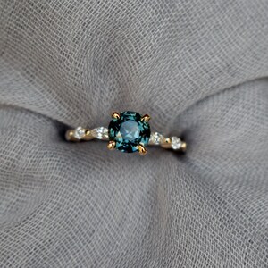 May include: A gold ring with a round, teal blue gemstone surrounded by smaller, clear gemstones.