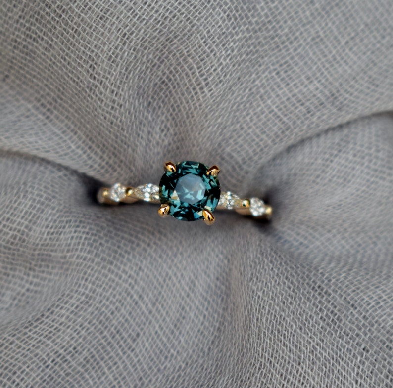 May include: A gold ring with a round, teal blue gemstone surrounded by smaller, clear gemstones.