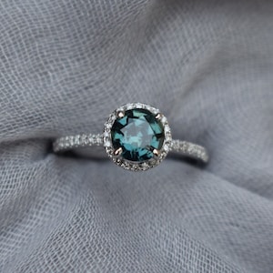 May include: A silver ring featuring a round, dark blue gemstone encircled by a halo of smaller diamonds.