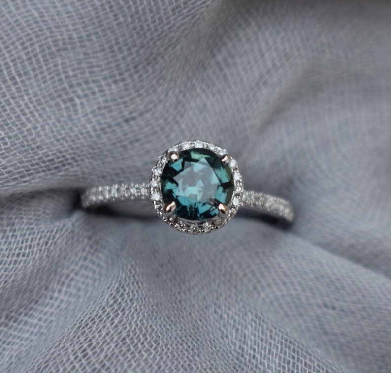 May include: A silver ring featuring a round, dark blue gemstone encircled by a halo of smaller diamonds.