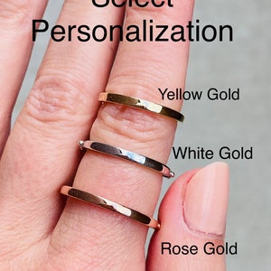May include: Three gold rings stacked on a finger. The top ring is yellow gold, the middle ring is white gold, and the bottom ring is rose gold. The text "Select Personalization" is at the top of the image.