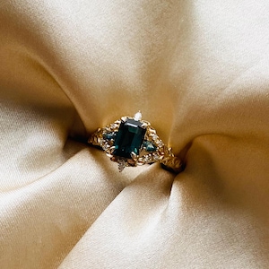 May include: A gold ring with a large emerald green gemstone surrounded by smaller diamonds. The ring has a detailed floral design.