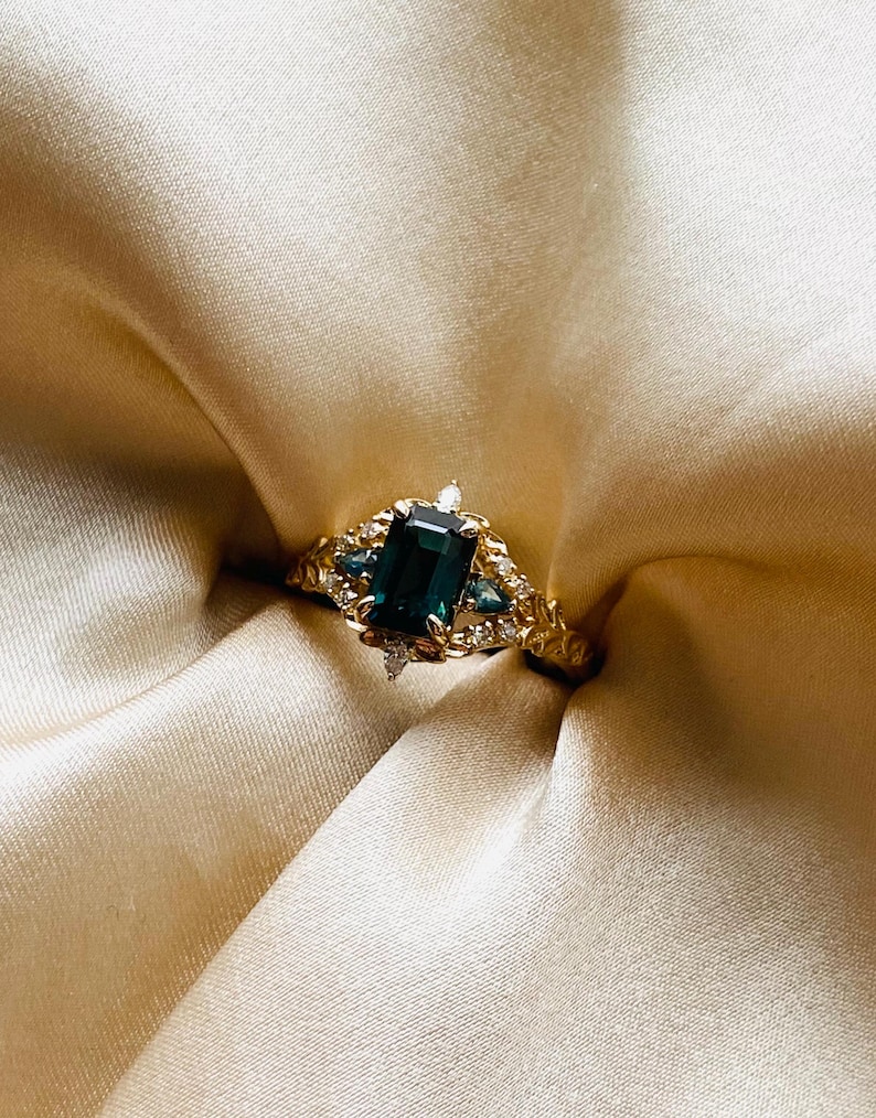 May include: A gold ring with a large emerald green gemstone surrounded by smaller diamonds. The ring has a detailed floral design.