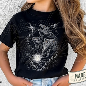 Op de afbeelding: Een zwart T-shirt met korte mouwen en een grafische print van drie leguanen omringd door bliksemschichten en een gloeiende maan. Het shirt heeft een ronde hals en is gemaakt van effen zwarte stof. Het ontwerp is gecentreerd op de voorzijde.