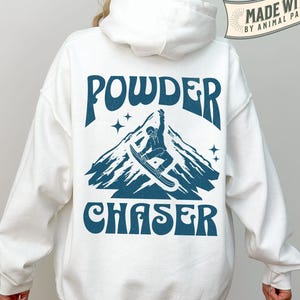 May include: White hoodie with a blue graphic on the back. The graphic features a mountain scene with a snowboarder and the words "POWDER CHASER". The hoodie also has the text "MADE WITH LOVE BY ANIMAL PARC APPAREL".