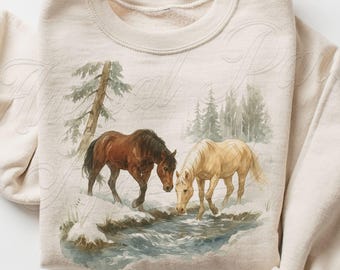 May include: Sand-colored sweatshirt featuring a watercolor painting of two horses by a stream in a snowy landscape. One horse is brown, the other is tan. The sweatshirt has a crew neck and long sleeves. The text "MADE WITH LOVE" is visible.