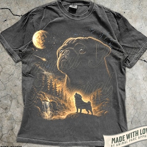 Könnte beinhalten: Ein pfefferfarbenes T-Shirt mit einem Grafikdruck, der die Silhouette eines Mopses auf einer Felsklippe bei einem Wasserfall und Tannen zeigt, sowie einen großen Mopskopf am Nachthimmel über einem Mond und einer Sternschnuppe in Goldgelb.