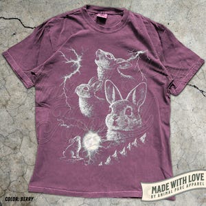 Pode incluir: Camiseta cor de berry com um gr&aacute;fico de coelhos, raios e uma lua cheia. O design inclui o texto "Made with Love by Animal Parc Apparel" em uma faixa. A cor da camiseta &eacute; identificada como "Berry".