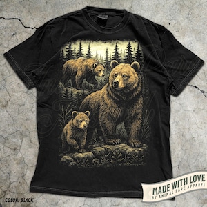 May include: Black t-shirt featuring a detailed illustration of a bear family in a forest setting. The design includes a large bear with two cubs, set against a backdrop of trees. The shirt has the text "MADE WITH LOVE BY ANIMAL PARC APPAREL".