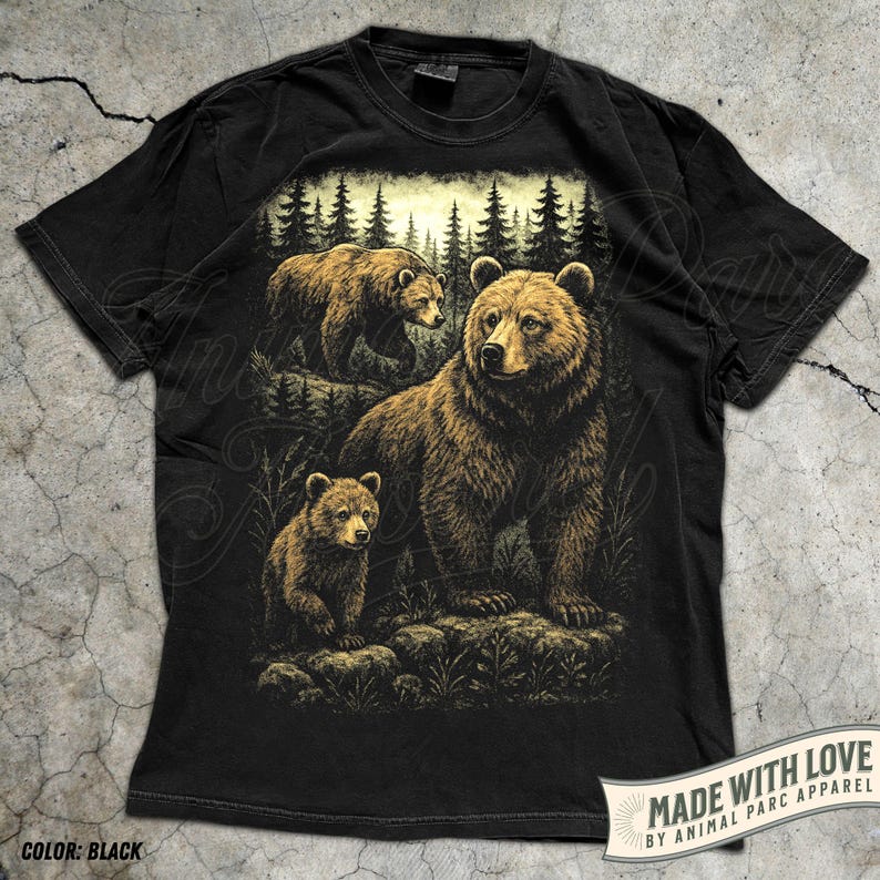 May include: Black t-shirt featuring a detailed illustration of a bear family in a forest setting. The design includes a large bear with two cubs, set against a backdrop of trees. The shirt has the text "MADE WITH LOVE BY ANIMAL PARC APPAREL".