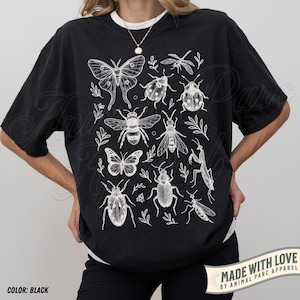 May include: Black t-shirt with a white insect and botanical illustration. The design features a butterfly, bee, dragonfly, ladybug, and other insects. The text "MADE WITH LOVE BY ANIMAL PARC APPAREL" is visible.