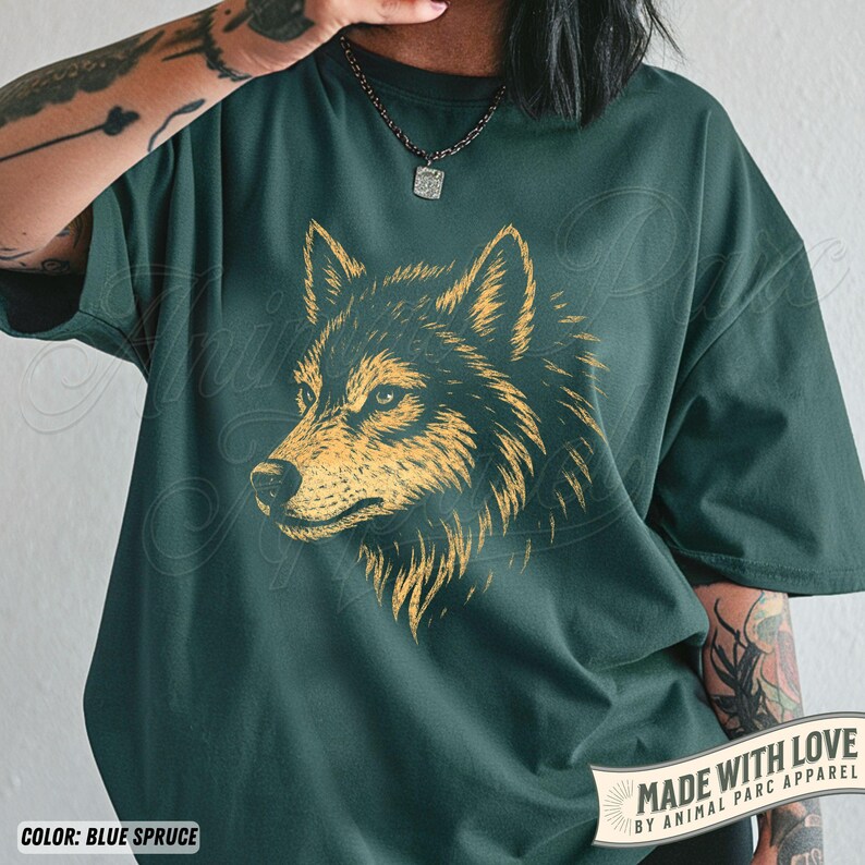 May include: Blue spruce t-shirt featuring a detailed golden wolf head graphic. The design showcases the wolf's profile with intricate fur details. The shirt includes the text "MADE WITH LOVE BY ANIMAL PARC APPAREL".
