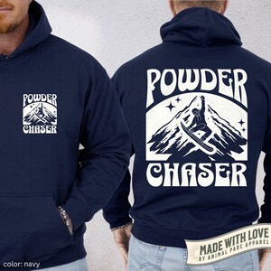 May include: Navy blue hoodie featuring a white mountain and snowboarder graphic, with the words "POWDER CHASER". The hoodie has a front pocket and a drawstring hood. The colour is navy.